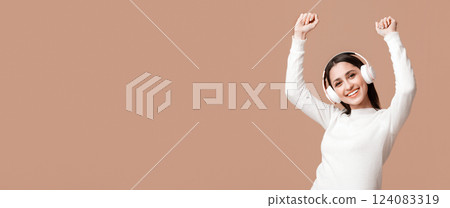 Portrait of joyful arabic girl in headphones dancing and enjoying her favorite music over yellow studio background with empty space 124083319