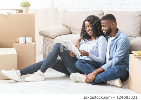 Setting up new appartment. Young african woman showing her man ideas for interior, using digital tablet, empty space 124083321