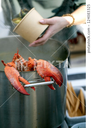 European street food festival. Large pot seafood soup displayed market counter cooked lobster balanced edge. Customers gathered around examining delicious seafood broth market setting restaurant 124083325