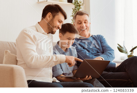 Boy Using Laptop Sitting Between Father And Grandpa Doing Homework Online On Sofa At Home. Selective Focus 124083339
