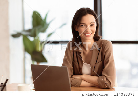Happy Office Worker. Portrait of confident female manager sitting at desk, folding arms, looking at camera, copyspace 124083375
