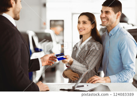 Young Couple Buying Car Giving Seller Credit Card Standing In Auto Dealership Office. Selective Focus 124083389