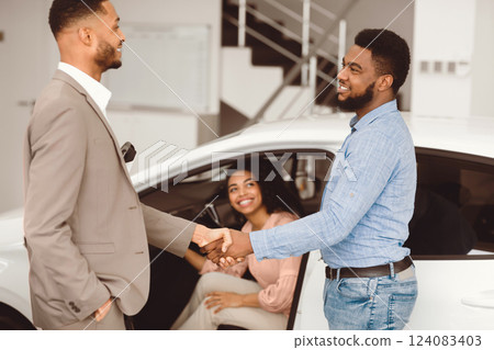 Car Seller Shaking Hands With Buyers After Successful Deal Selling Auto In Dealership Center. Selective Focus Car Seller Shaking Hands With Buyers After Successful Deal Selling Auto In Dealership Center. Selective Focus 124083403