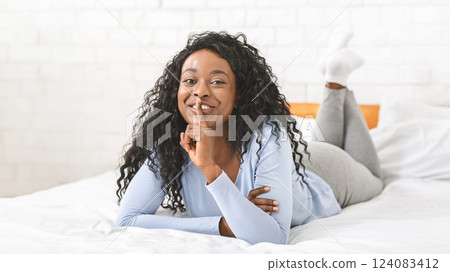 Flirting afro girl laying on bed and showing silence sign, touching lips with finger 124083412