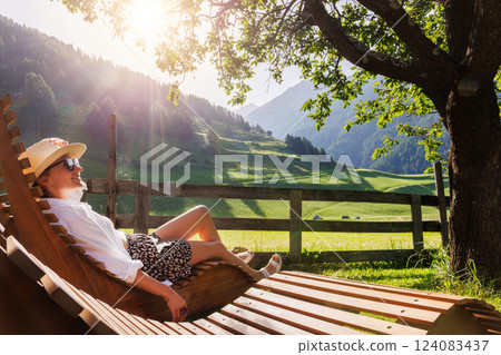 Portrait happy smiling woman sunglasses enjoy relax on wooden lounge chair outdoors in alpine countryside resort hotel garden warm sunny summer day. Alpine rural eco-tourism vacation retreat outdoors Portrait happy smiling woman sunglasses enjoy relax on wooden lounge chair outdoors in alpine countryside resort hotel garden warm sunny summer day. Alpine rural eco-tourism vacation retreat outdoors 124083437