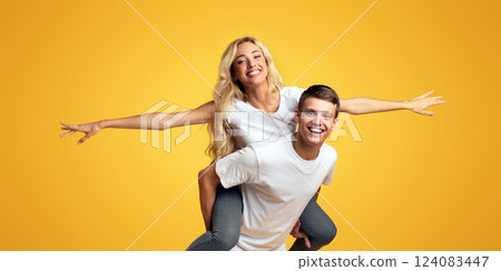 Young romantic couple fooling over yellow background, girl riding her boyfriend. Panorama with copy space 124083447