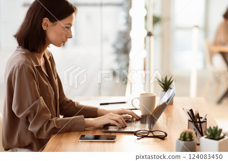 Concentrated At Work. Side view of focused girl working on laptop, sitting near window in creative office or cafe 124083450