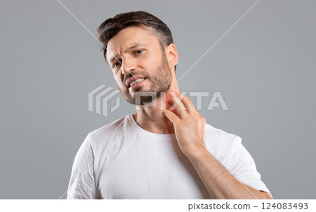 Middle aged bearded man scratching highlighted with red neck on grey studio background, copy space. Annoyed man suffering from itch, having rash on his neck. Allergic reaction, eczema concept 124083493