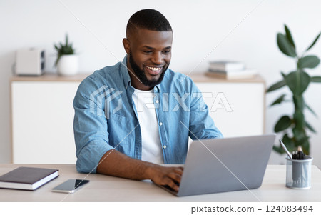 Distance Job. Millennial African American Man Working Online On Computer At Home Office, Handsome Smiling Black Freelancer Guy Sitting At Desk And Looking At Laptop Screen, Free Space 124083494