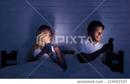 Cheating Concept. Unfaithful Husband Chatting On Cellphone Lying With Wife In Bed At Night. Selective Focus, Low Light 124083507