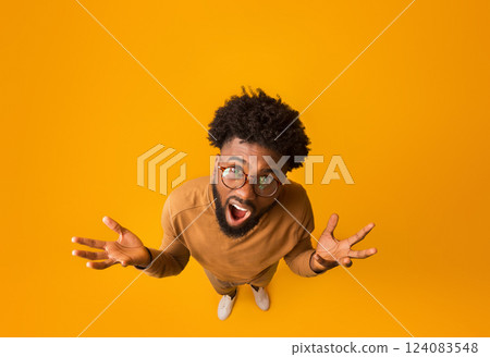 Top view of african american indignant man wearing glasses, raising hands and screaming, full body over orange background Top view of african american indignant man wearing glasses, raising hands and screaming, full body over orange background 124083548
