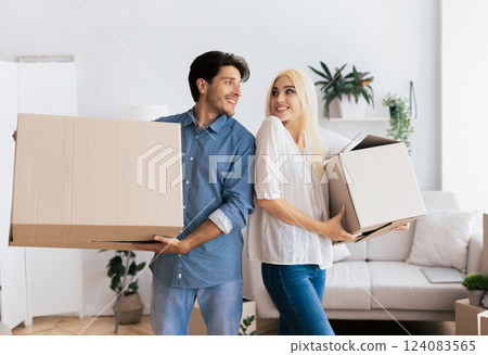 A couple smiling and holding cardboard boxes in a new house. A couple smiling and holding cardboard boxes in a new house. 124083565