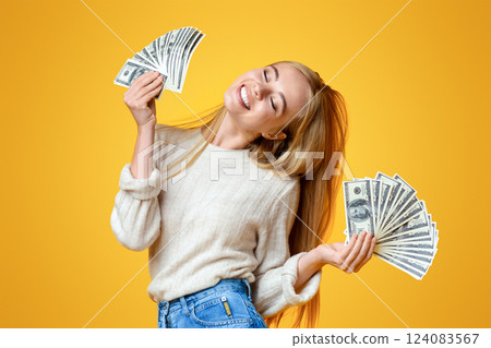 Blissful millennial girl holding lots of money and enjoying success on orange studio background, panorama with free space 124083567