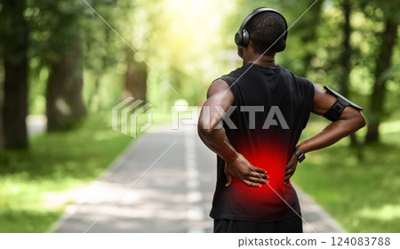 Back view of black sportsman touching sore zone on his back, having back pain during jogging by park, empty space 124083788