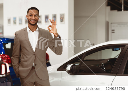 Car Sales. Smiling Black Salesman Gesturing Okay Standing In Luxury Auto Store. Free Space For Text 124083790