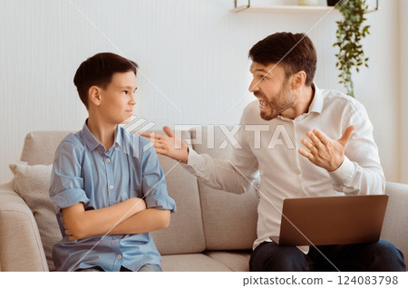 Aggressive Father. Angry Dad Yelling At Offended Son Working On Laptop Sitting On Couch Indoor. Selective Focus Aggressive Father. Angry Dad Yelling At Offended Son Working On Laptop Sitting On Couch Indoor. Selective Focus 124083798