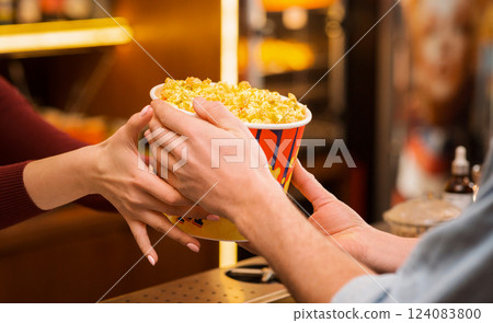 Cinema and entertainment. Young man buying popcorn from saleswoman in movie theater lobby, closeup of hands 124083800
