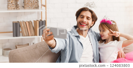 Cheerful family taking selfie on phone together at home, father and daughter dressing as princesses Cheerful family taking selfie on phone together at home, father and daughter dressing as princesses 124083803