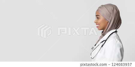 Profile portrait of smiling afro muslim female doctor in hijab and lab coat with stethoscope looking at copy space over light background, panorama 124083937