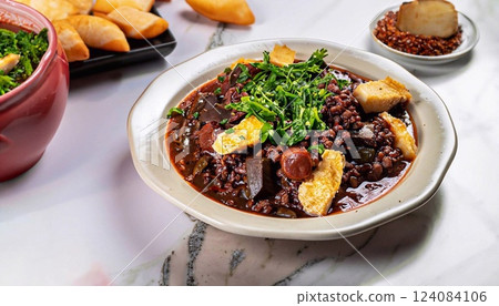 Feijoada garnished with greens in a plate on a white marble serving table 124084106