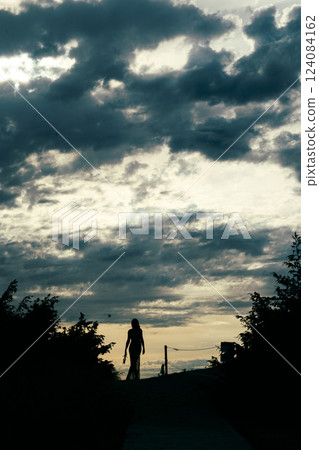 Silhouette of a Woman Walking at Sunset with Dramatic Clouds 124084162