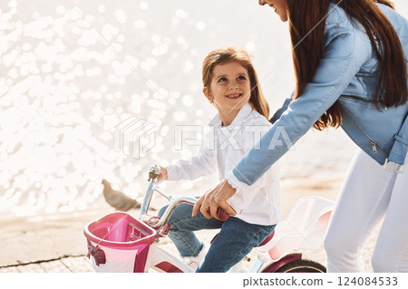 Learning how to drive. Mother with her young daughter is with bicycle outdoors together Learning how to drive. Mother with her young daughter is with bicycle outdoors together 124084533