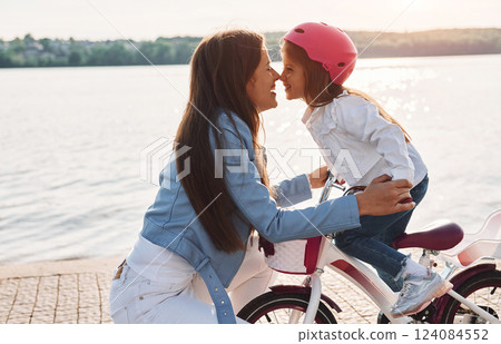 Woman care for her little girl. Mother with her young daughter is with bicycle outdoors together Woman care for her little girl. Mother with her young daughter is with bicycle outdoors together 124084552