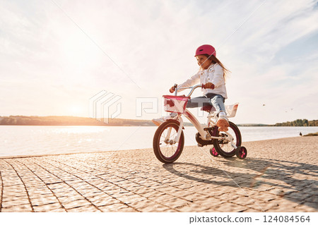 Having fun near the lake. Happy little girl riding a bicycle outdoors in summer Having fun near the lake. Happy little girl riding a bicycle outdoors in summer 124084564