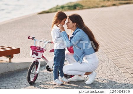 Woman care for her little girl. Mother with her young daughter is with bicycle outdoors together 124084569
