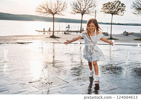 Happy little girl having fun outdoors in the fountain near the lake at summer Happy little girl having fun outdoors in the fountain near the lake at summer 124084613