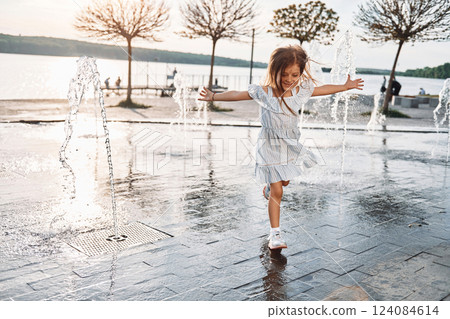 Happy little girl having fun outdoors in the fountain near the lake at summer 124084614