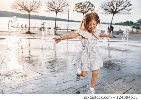 Happy little girl having fun outdoors in the fountain near the lake at summer Happy little girl having fun outdoors in the fountain near the lake at summer 124084615