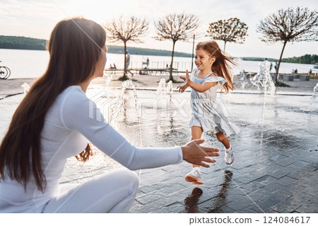 Little girl with her mother having fun outdoors in fountain near the lake Little girl with her mother having fun outdoors in fountain near the lake 124084617