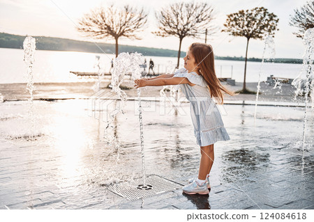 Happy little girl having fun outdoors in the fountain near the lake at summer Happy little girl having fun outdoors in the fountain near the lake at summer 124084618