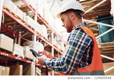 With tablet. Employee in uniform is working in the storage at daytime 124085048