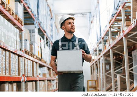 Walking with white box in hands. Employee in uniform is working in the storage at daytime Walking with white box in hands. Employee in uniform is working in the storage at daytime 124085105
