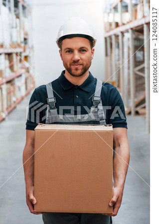 With delivery package in hands. Employee in uniform is working in the storage at daytime 124085117