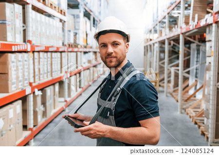 Side view of man that holding tablet. Employee in uniform is working in the storage at daytime 124085124