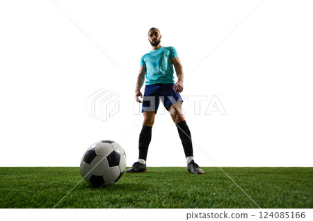 Low-angle view of football player standing over ball on green field, exuding confidence and dominance before action. Low-angle view of football player standing over ball on green field, exuding confidence and dominance before action. 124085166