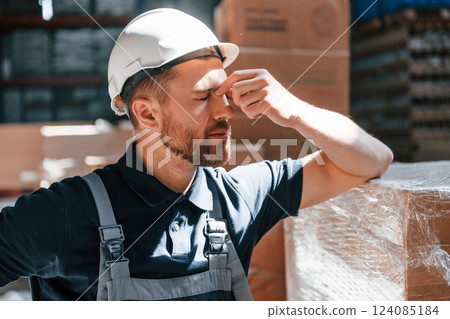 Taking a break. Tired employee in uniform is working in the storage at daytime Taking a break. Tired employee in uniform is working in the storage at daytime 124085184