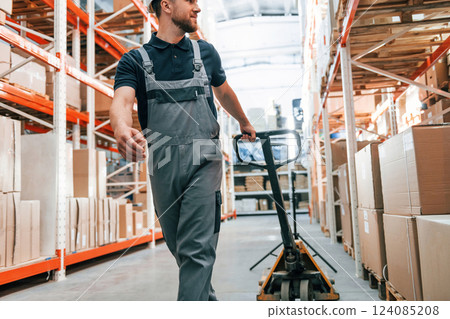 Walking with platform trolley. Employee in uniform is working in the storage at daytime 124085208