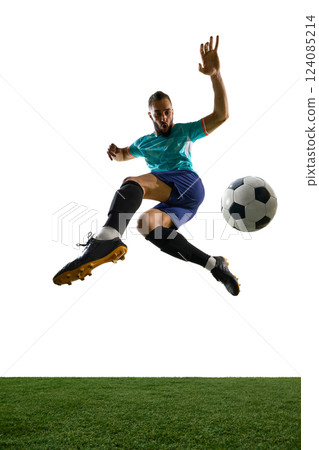 Side view of football player in blue uniform airborne, preparing to strike ball with intense focus and athleticism on green field. Side view of football player in blue uniform airborne, preparing to strike ball with intense focus and athleticism on green field. 124085214