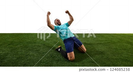 Male footballer celebrating victory, kneeling on grass, fists clenched, roaring in triumph, emotions pouring after decisive match. Male footballer celebrating victory, kneeling on grass, fists clenched, roaring in triumph, emotions pouring after decisive match. 124085238