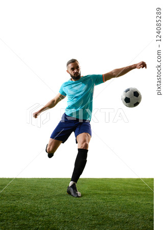 Focused footballer in blue uniform balancing ball mid-air, arms extended, preparing for powerful strike on green field against white background. Focused footballer in blue uniform balancing ball mid-air, arms extended, preparing for powerful strike on green field against white background. 124085289
