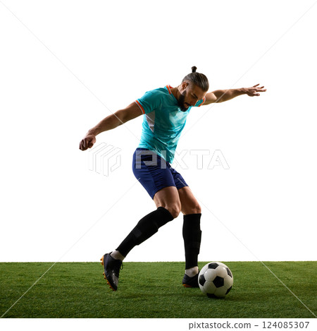 Side view dynamic photo of young football athlete, training kicks ball in motion on green stadium against white background. 124085307