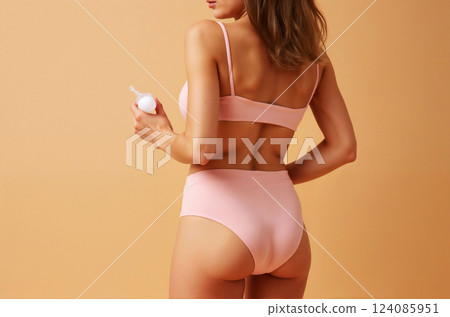 A woman is wearing a pink bikini and holding a bottle of lotion 124085951