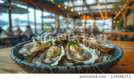 A bowl of fresh oysters on rice is presented at a lively outdoor restaurant adorned with ambient lighting during the evening. 124086251