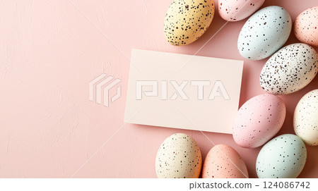 A top view of pastel Easter eggs with speckled patterns arranged on a soft pink background with a blank white card, leaving space for text or design. 124086742