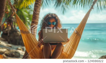 Relaxing in a hammock while working on a laptop near a beautiful beach under palm trees 124086822