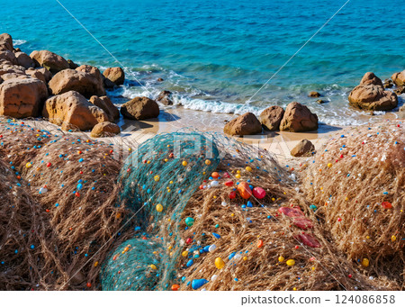 A beach with a rocky coast is littered with a net filled with colorful balls 124086858